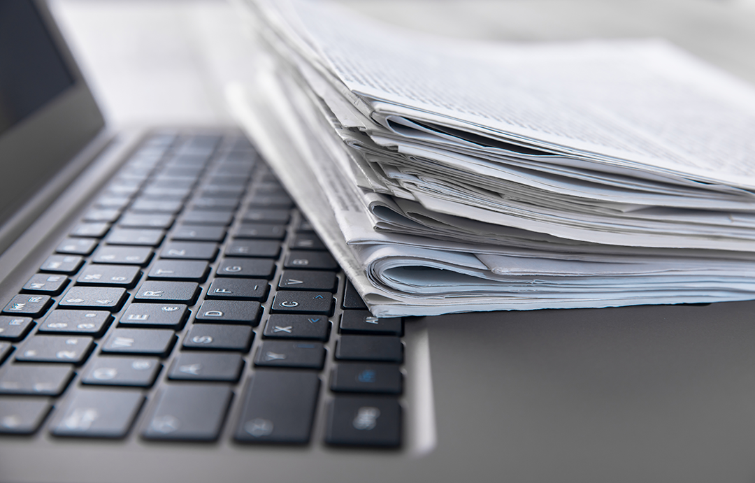 Laptop with small stack of newspapers